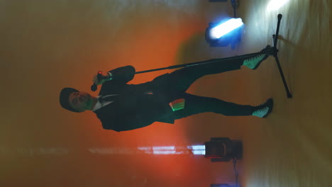 Vertical-video.-Incendiary-funny-Singer-in-stylish-clothes-dancing-and-singing-with-a-microphone-in-neon-color.-Jump-and-move-vigorously.-Pop-singer